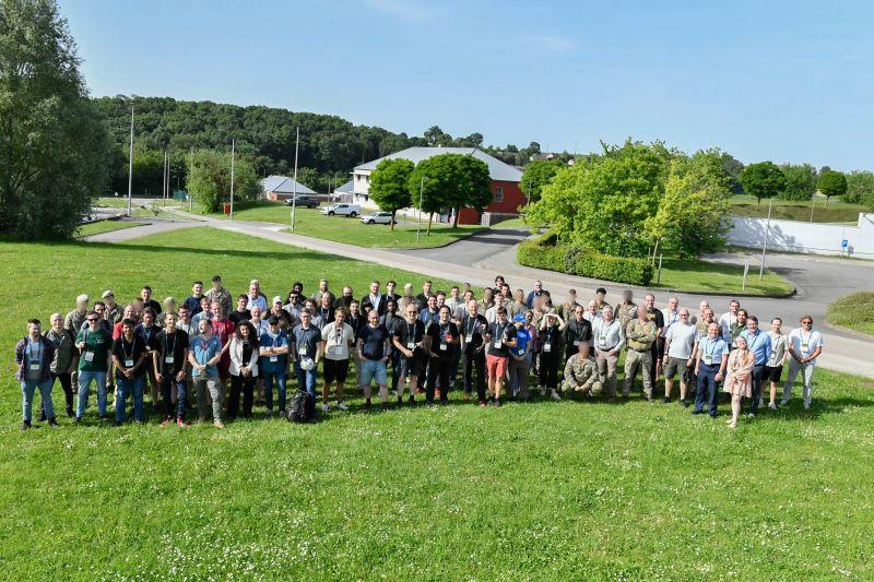 Group photo of all Battlefield of Things 3 participants at the Commando Training Center in Marche-les-Dames, Belgium, approximately 80 people standing on a grass field