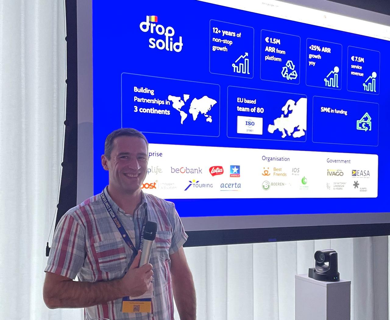 Frederik presenting on stage with Dropsolid slide showing 12+ years growth, 80 person team, clients including Beobank, Lotus, EASA