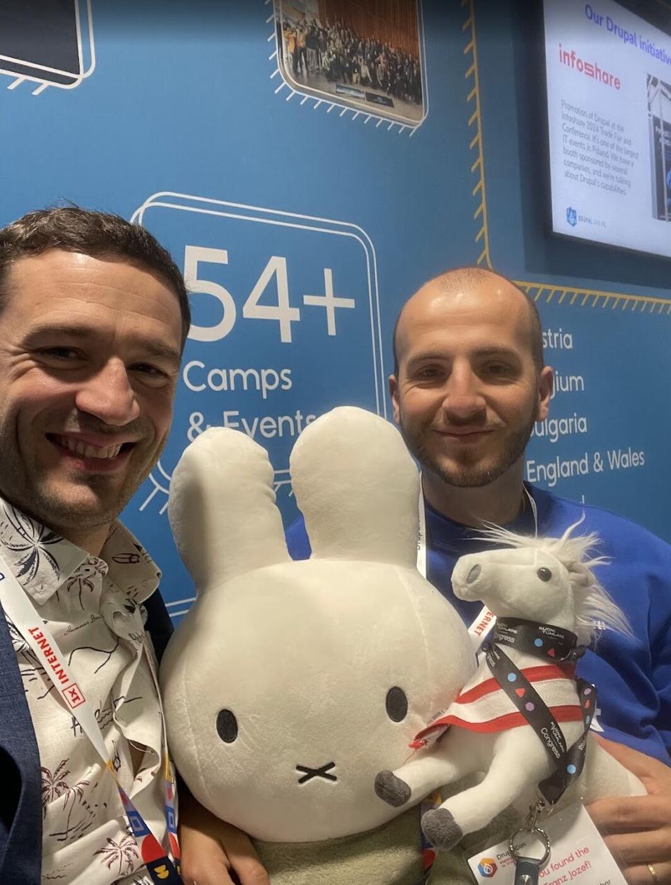 Frederik and a colleague holding Miffy and a horse at the Drupal booth