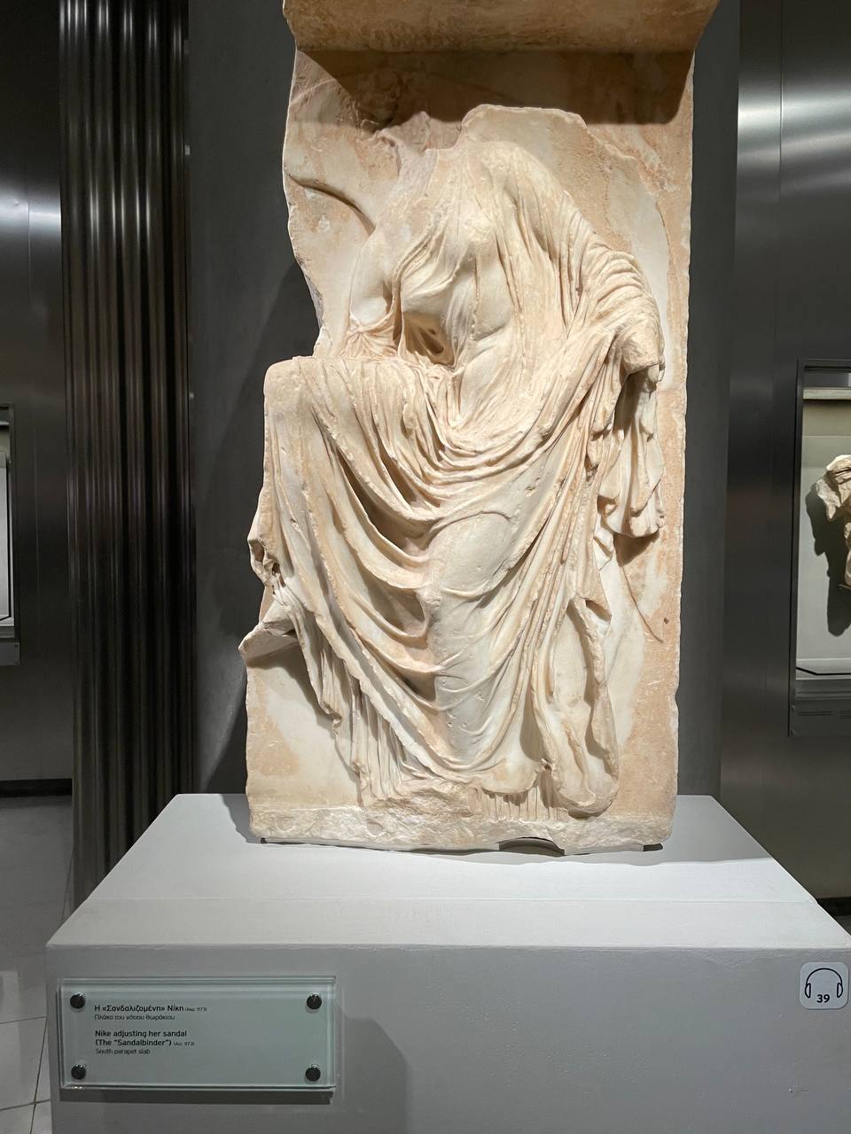 Marble relief known as 'Nike adjusting her sandal' or 'The Sandalbinder', from the south parapet slab of the Temple of Athena Nike on the Acropolis, circa 410 BCE, displayed at the Parthenon Museum in Athens