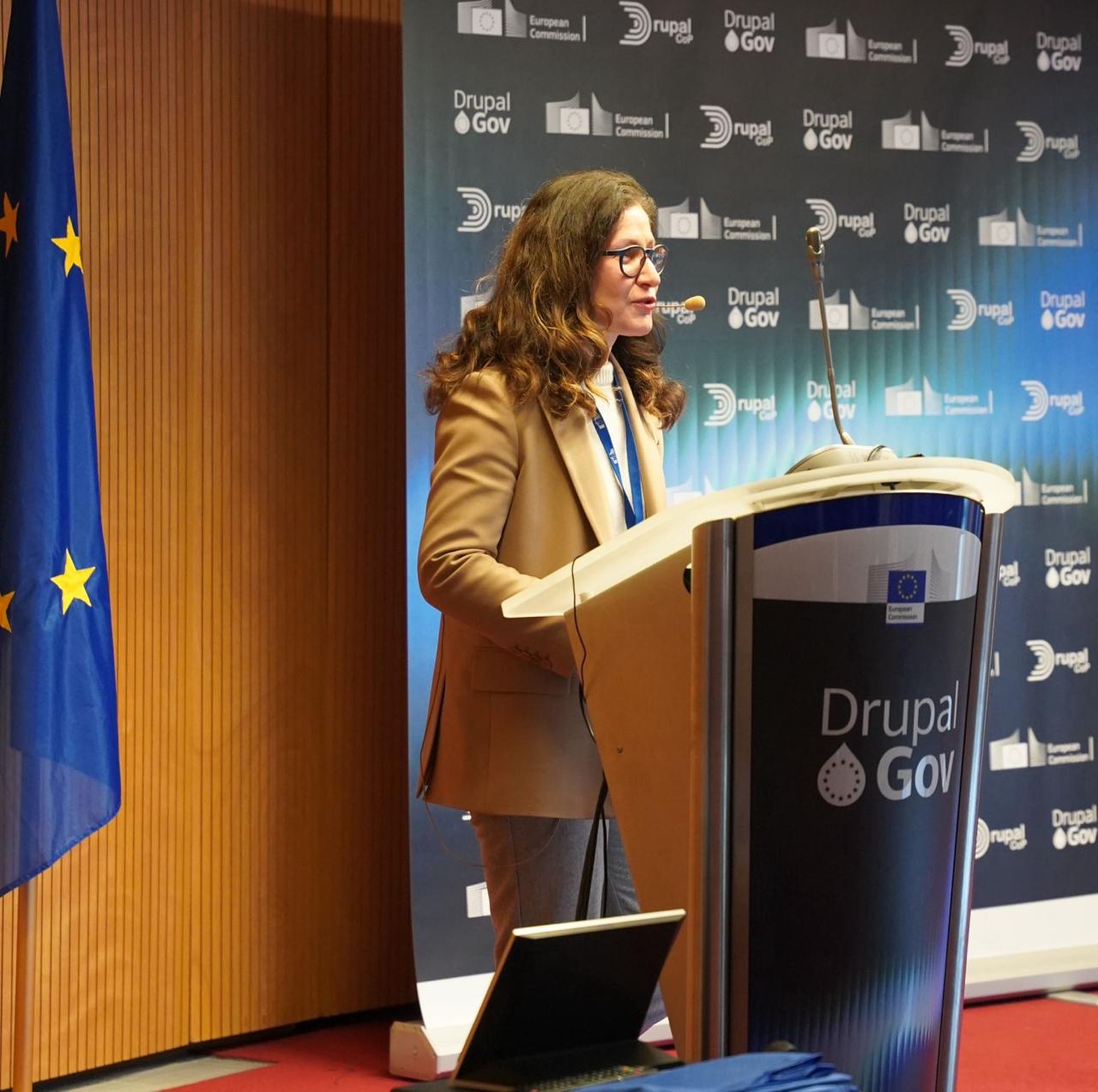 Speaker at the Drupal Gov podium with European Commission branding and EU flag
