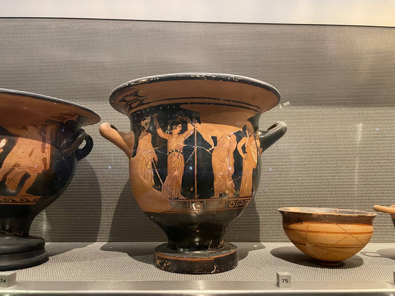 Ancient Greek red-figure pottery krater in a display case at the Parthenon Museum, showing figures in a ritual or mythological scene