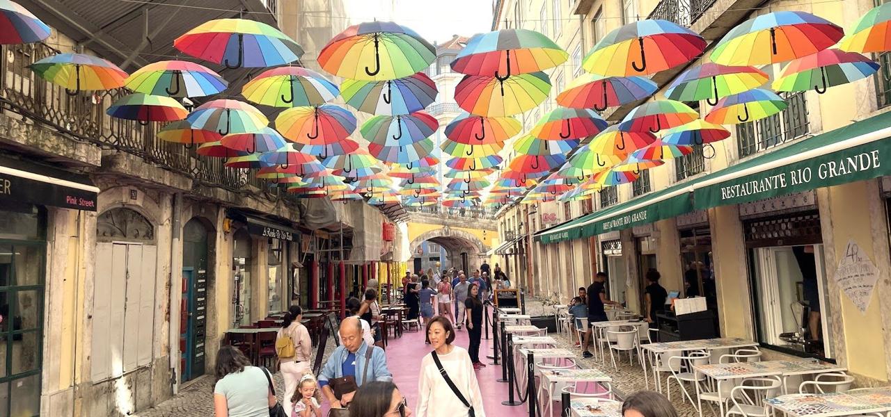 Pink Street in Lisbon with dozens of colourful umbrellas hanging overhead between the buildings