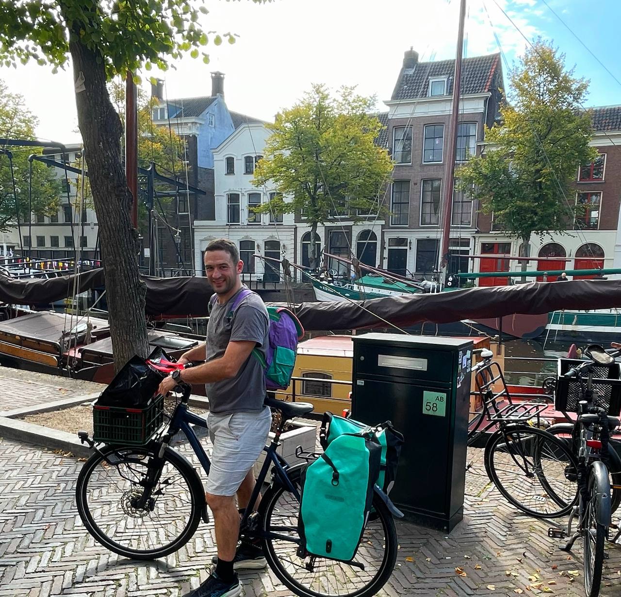 Frederik on a bike in Schiedam, picking up the speaker gifts, with historic Dutch canal houses and boats in the background