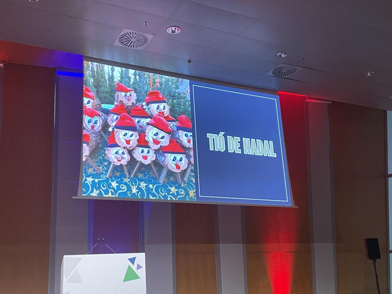 Conference slide showing TIÓ DE NADAL - rows of smiling Christmas logs with red hats