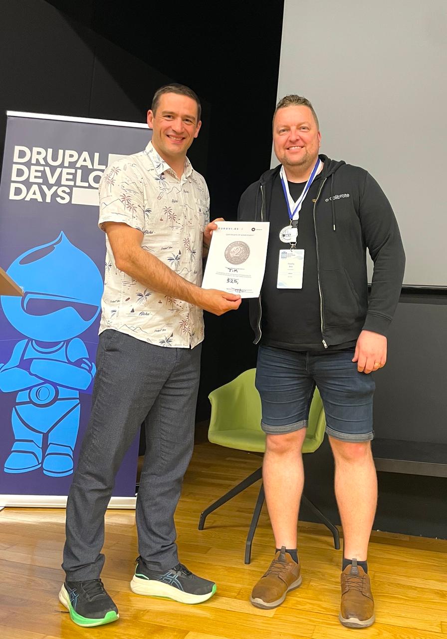 Frederik Wouters awarding the silver medal to Tim at the Vibe Coding Challenge prize ceremony, Drupal Developer Days Athens 2026 banner visible in background