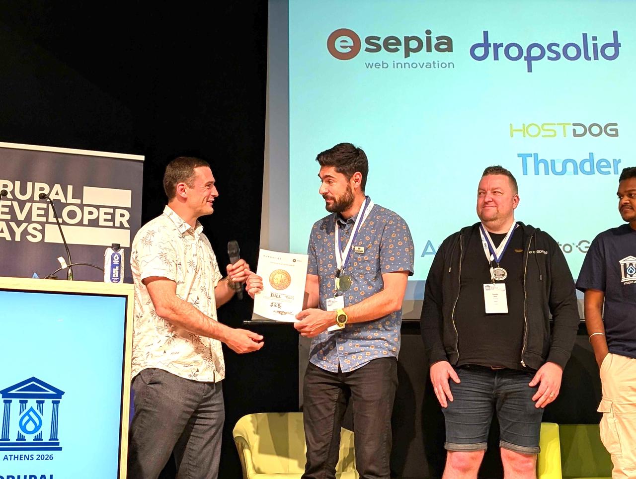Frederik Wouters presenting the gold medal and AI budget prize to Bill Seremetis on the main stage at Drupal Developer Days Athens 2026