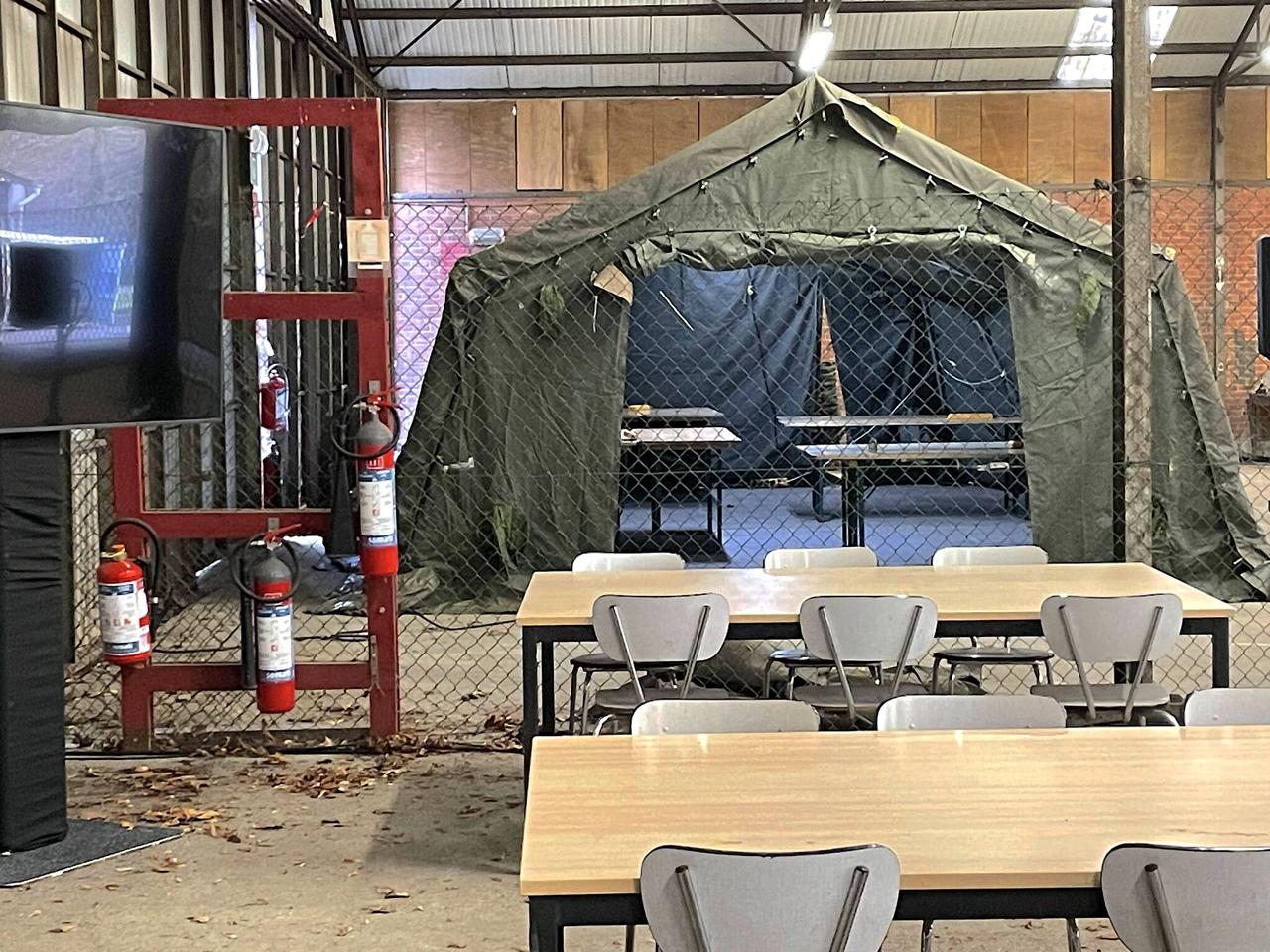 Inside the hackathon hall at Vlasmeer: military tent setup behind chain-link fencing, folding tables in foreground