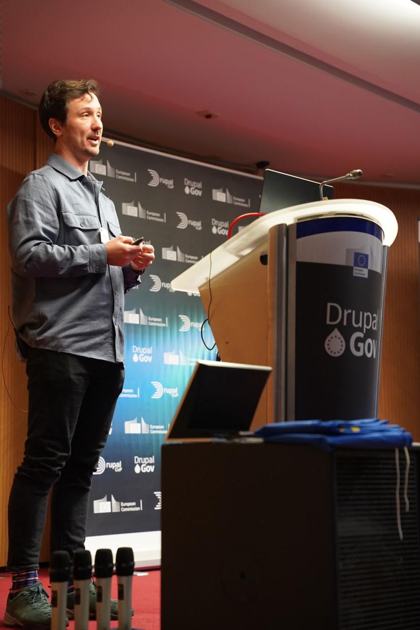Speaker presenting on stage in front of the Drupal Gov and European Commission backdrop