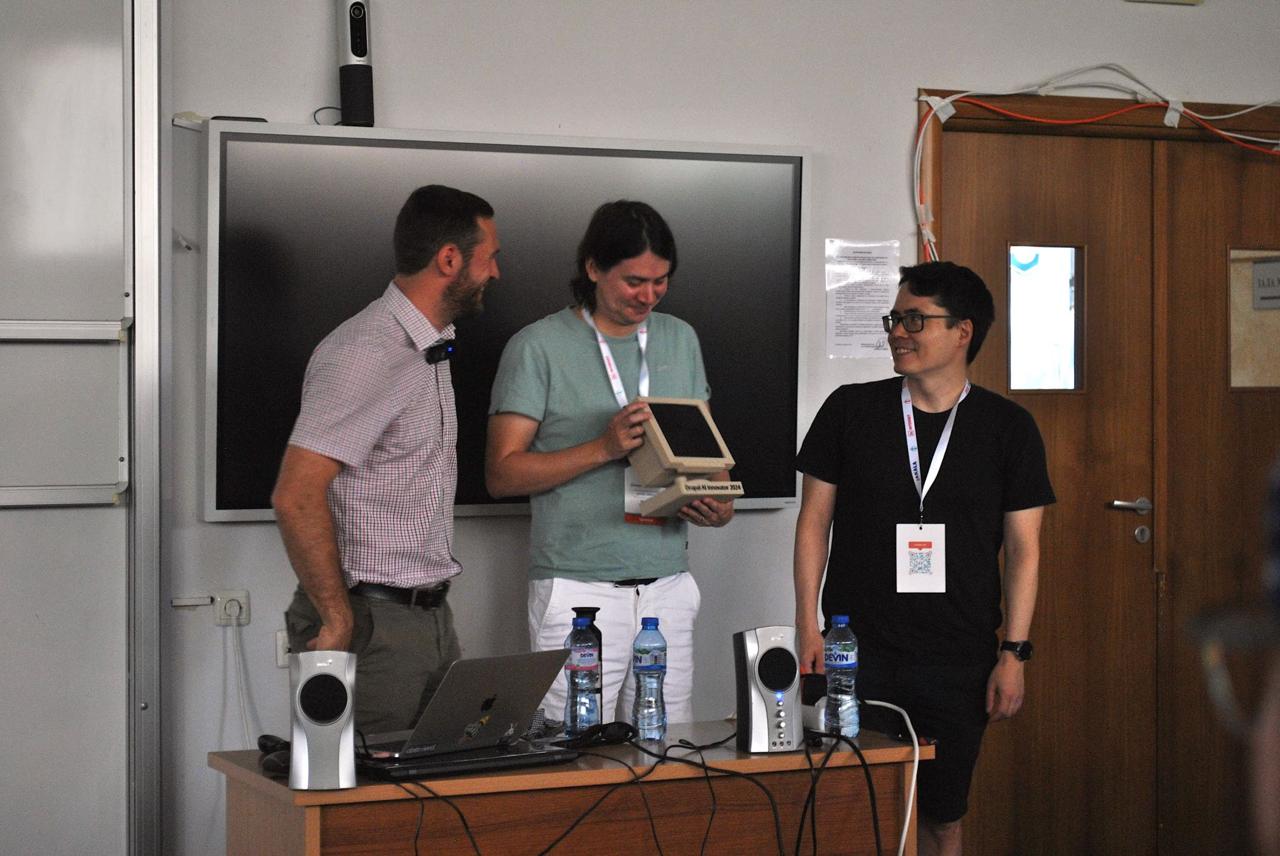 Prize ceremony: Frederik handing a wooden trophy to the winner, a third person smiling alongside
