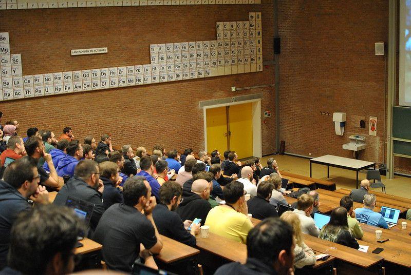 Packed lecture hall with periodic table on the wall - attendees following a session