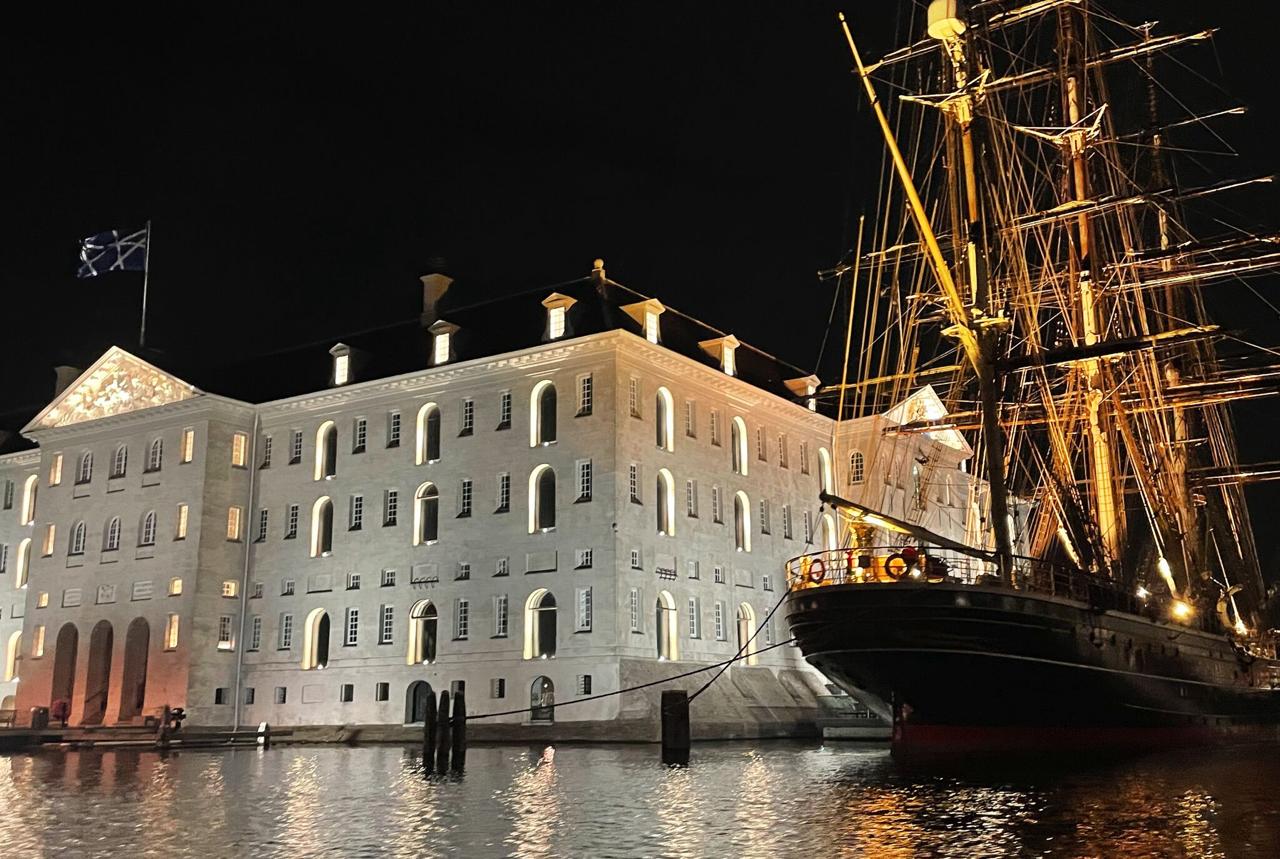 Amsterdam Scheepvaartmuseum at night with a tall ship moored alongside