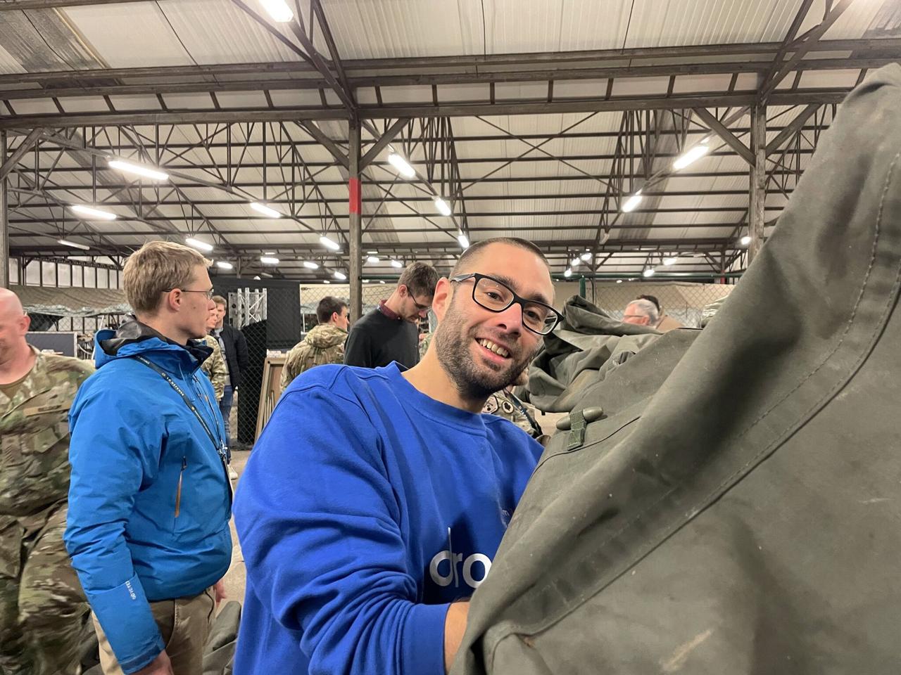 Jasper in Dropsolid sweater helping examine military equipment alongside other participants and soldiers